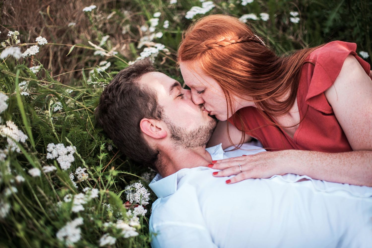 Couple lying in field of white flowers sharing intimate moments.
