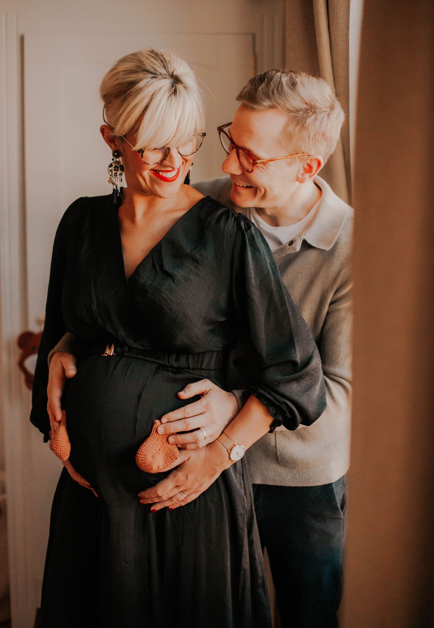 Intimate indoor maternity photo with couple embracing and sharing joyful laughter.