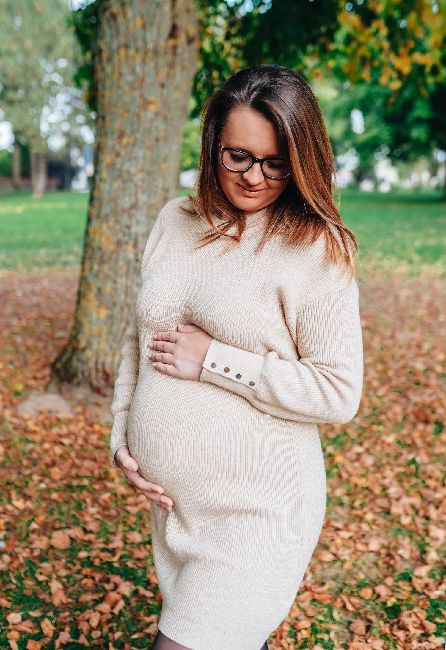 Maternity photos showing pregnant belly in cream sweater against autumn leaves.