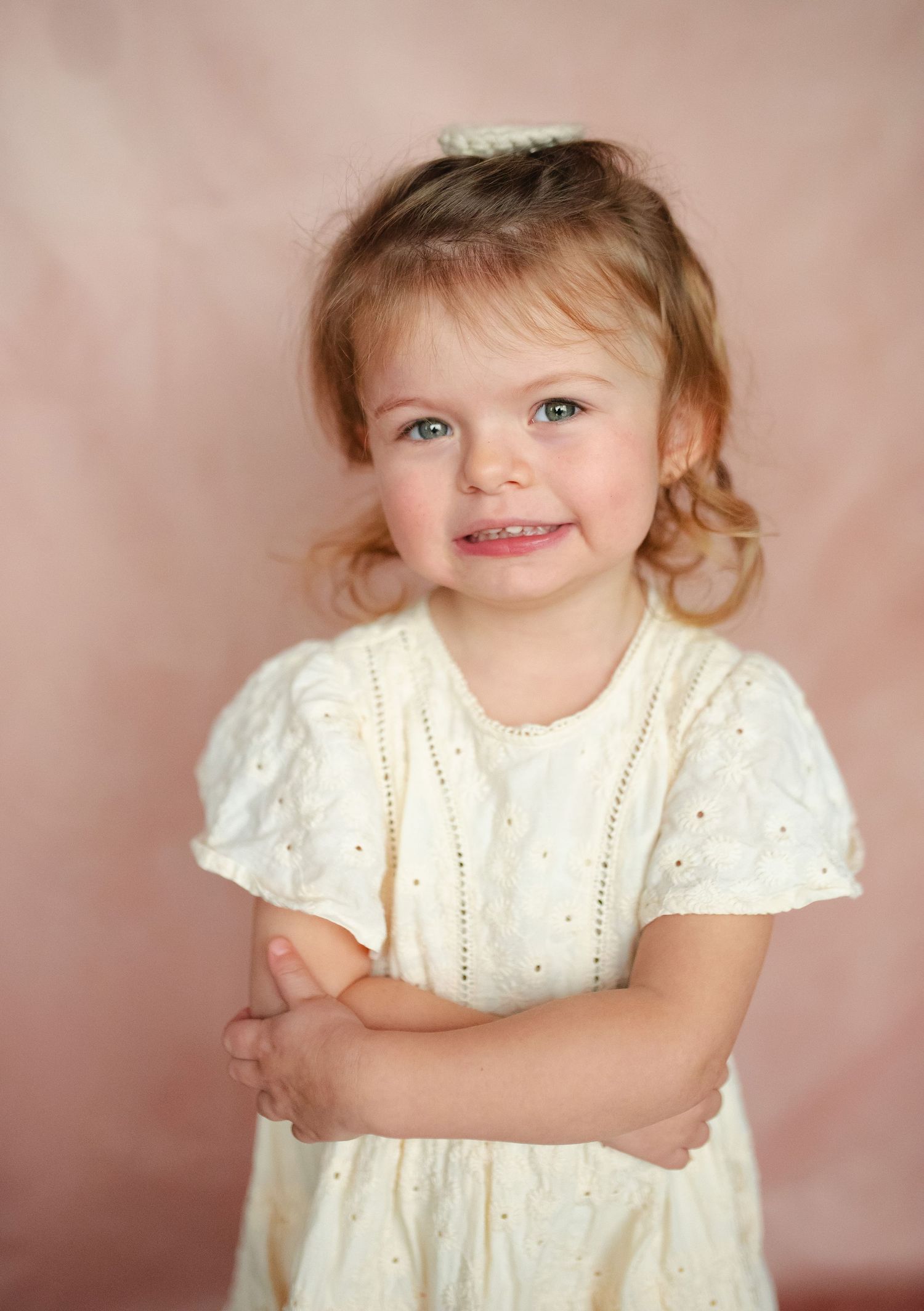 A series of studio portraits showing a small child wearing a white eyelet dress against a pink background.