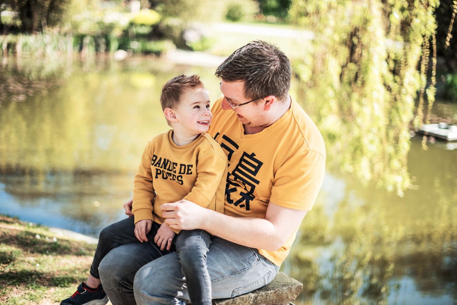 Intimate family moments captured by a pond with willow trees in background.