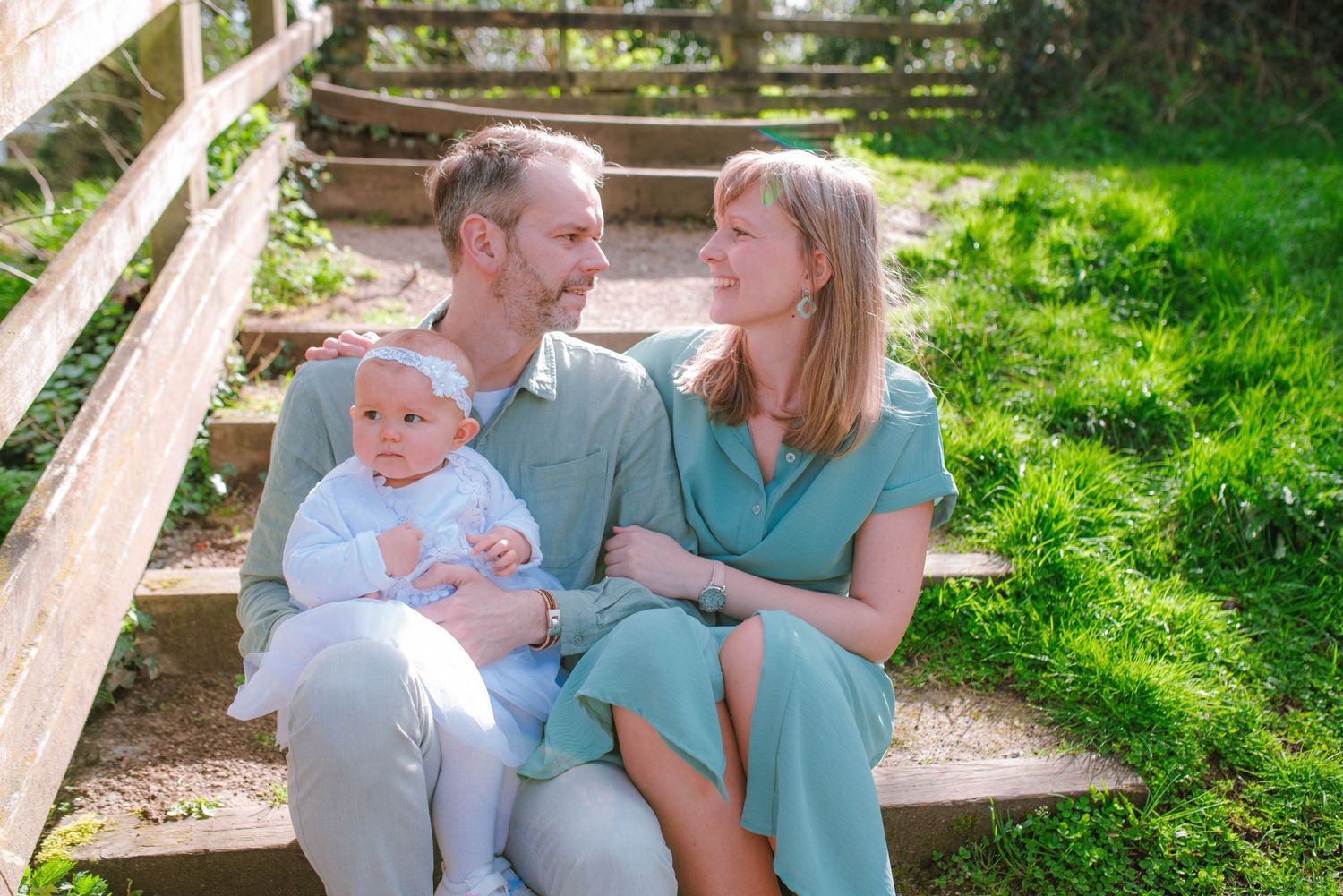 Family portrait in a sunlit garden setting wearing coordinated blue and gray outfits.