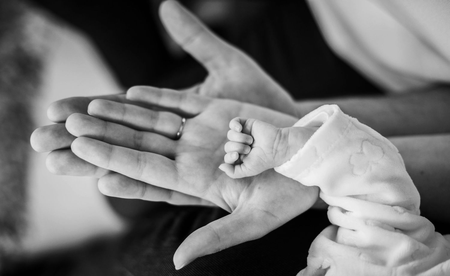 Close-up black and white images of hands holding newborn baby.
