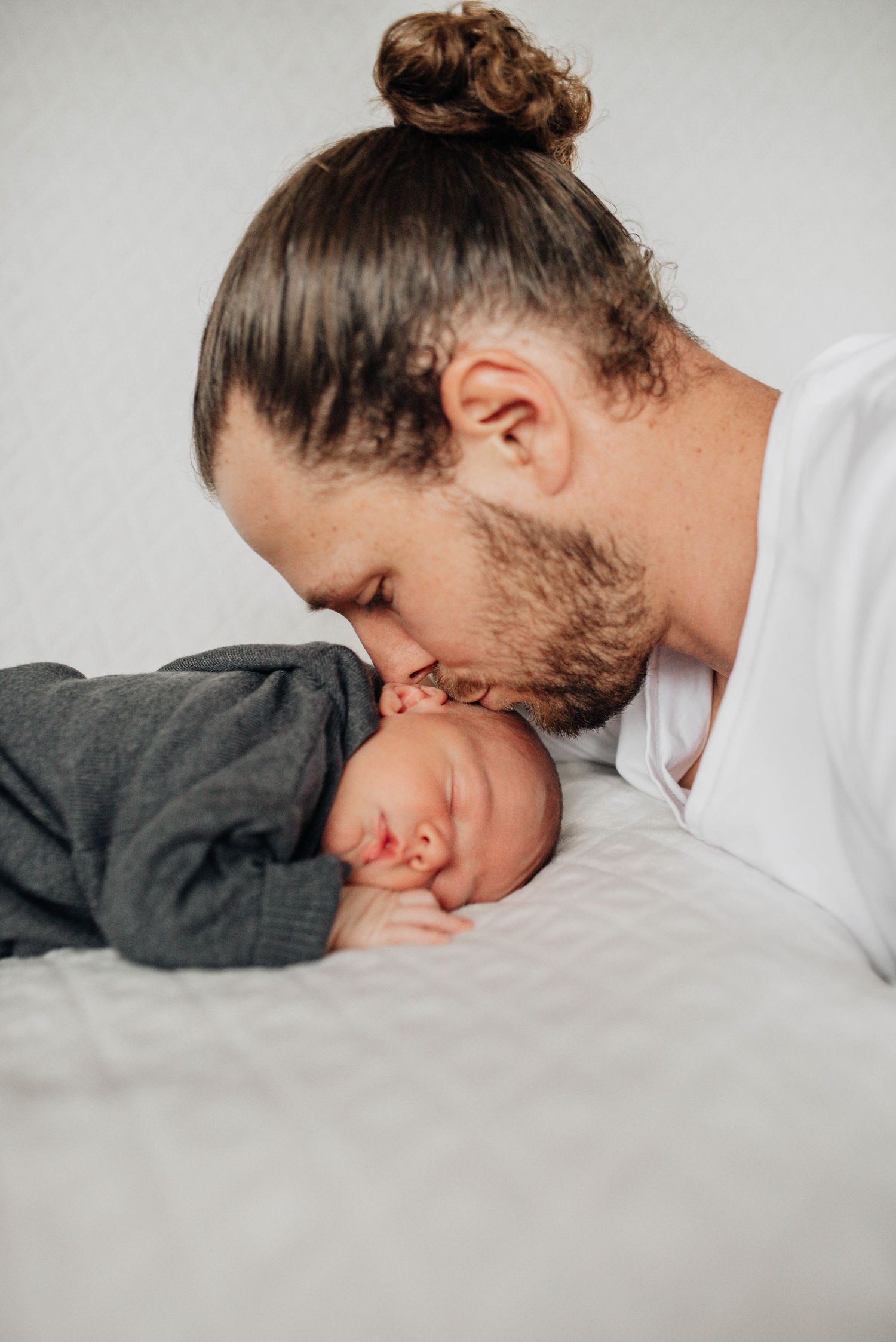 Intimate black and white portrait series showing tender moments between parent and child on white bedding.