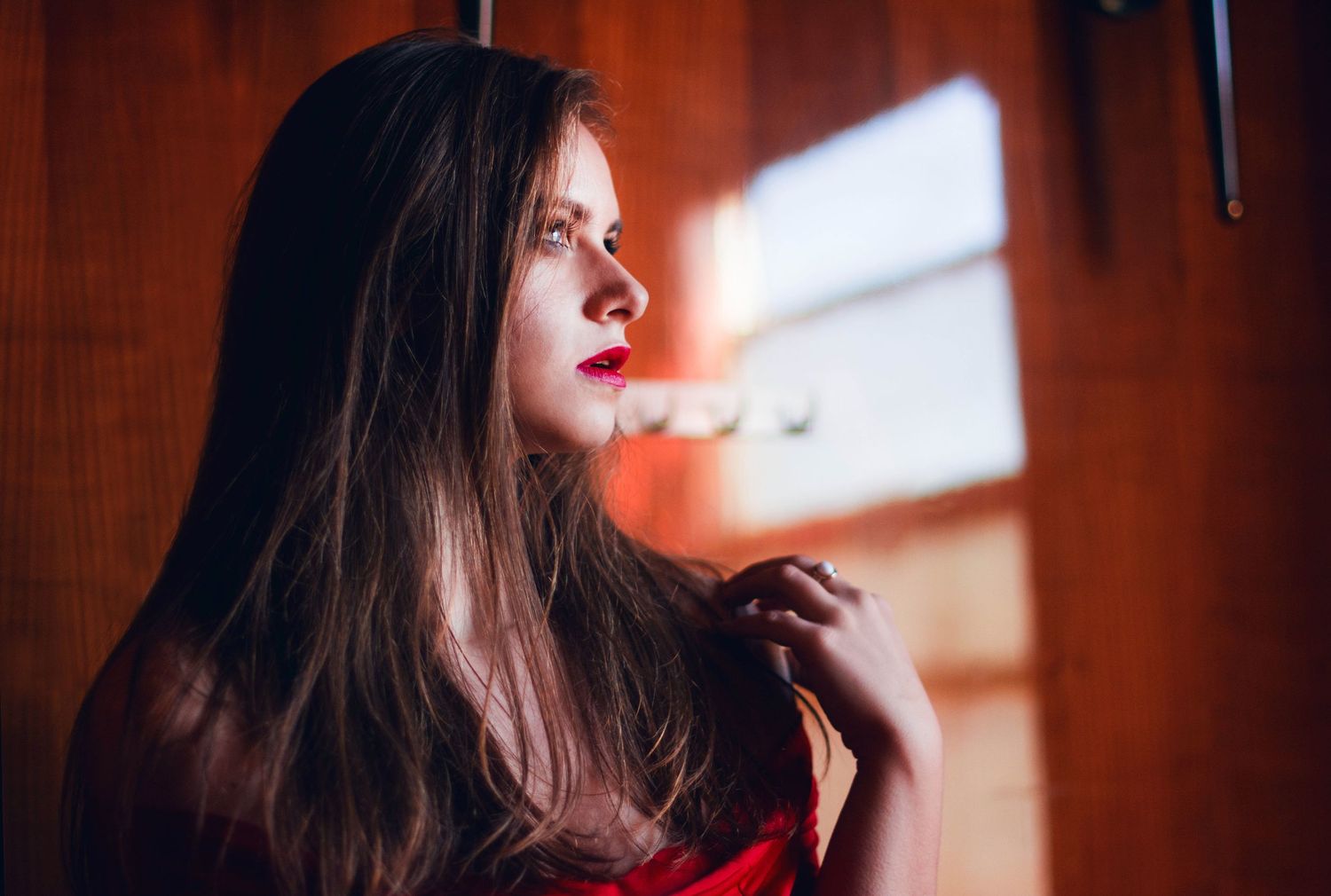 Moody indoor portrait with dramatic window lighting and red color accents.