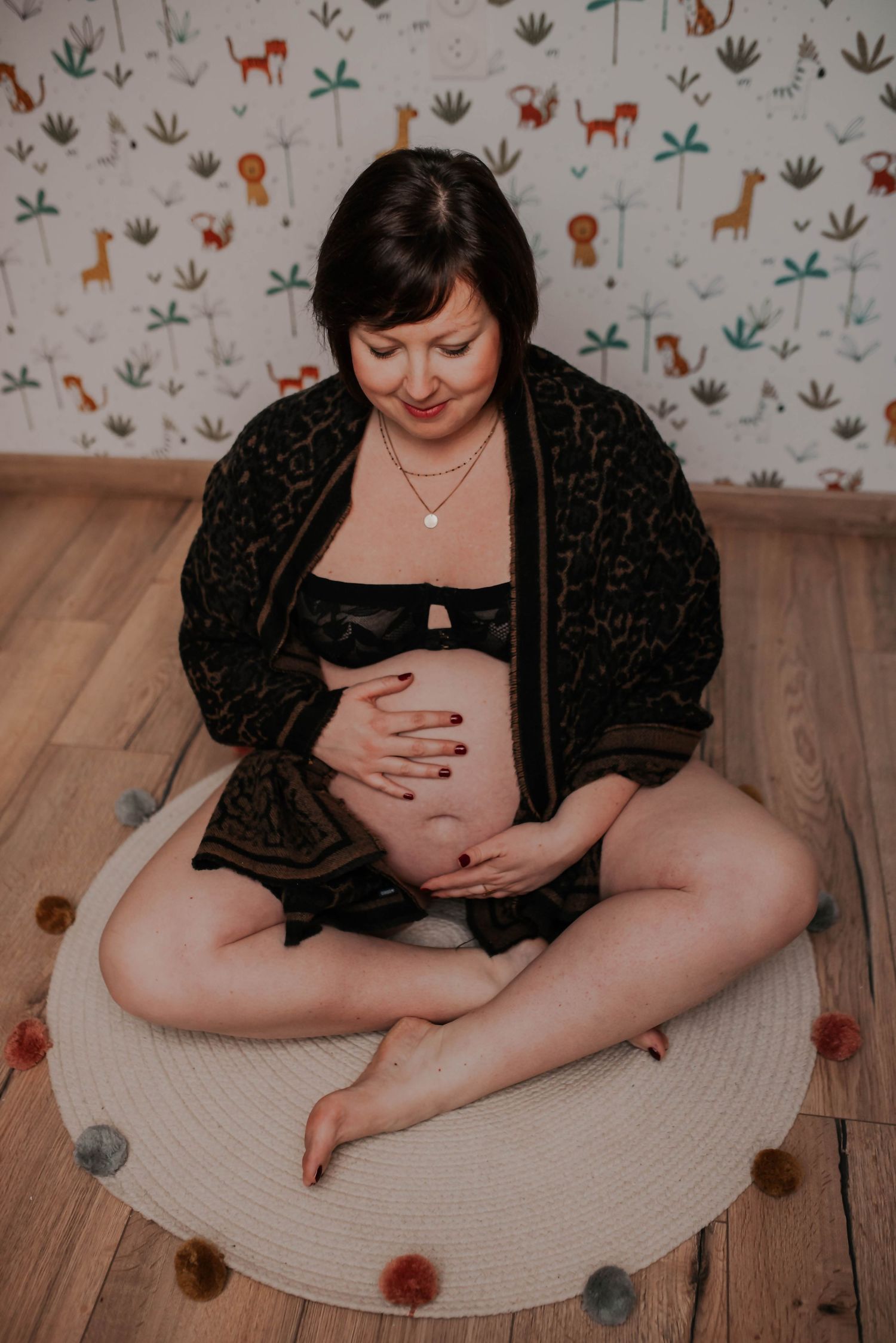 Indoor maternity photos on wooden floor with whimsical animal print wallpaper background.