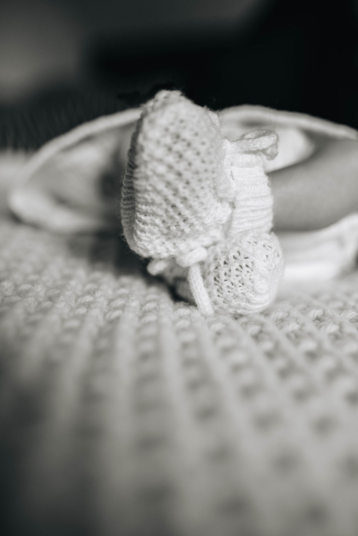 Close-up of delicate white knitted baby bootie on textured fabric.