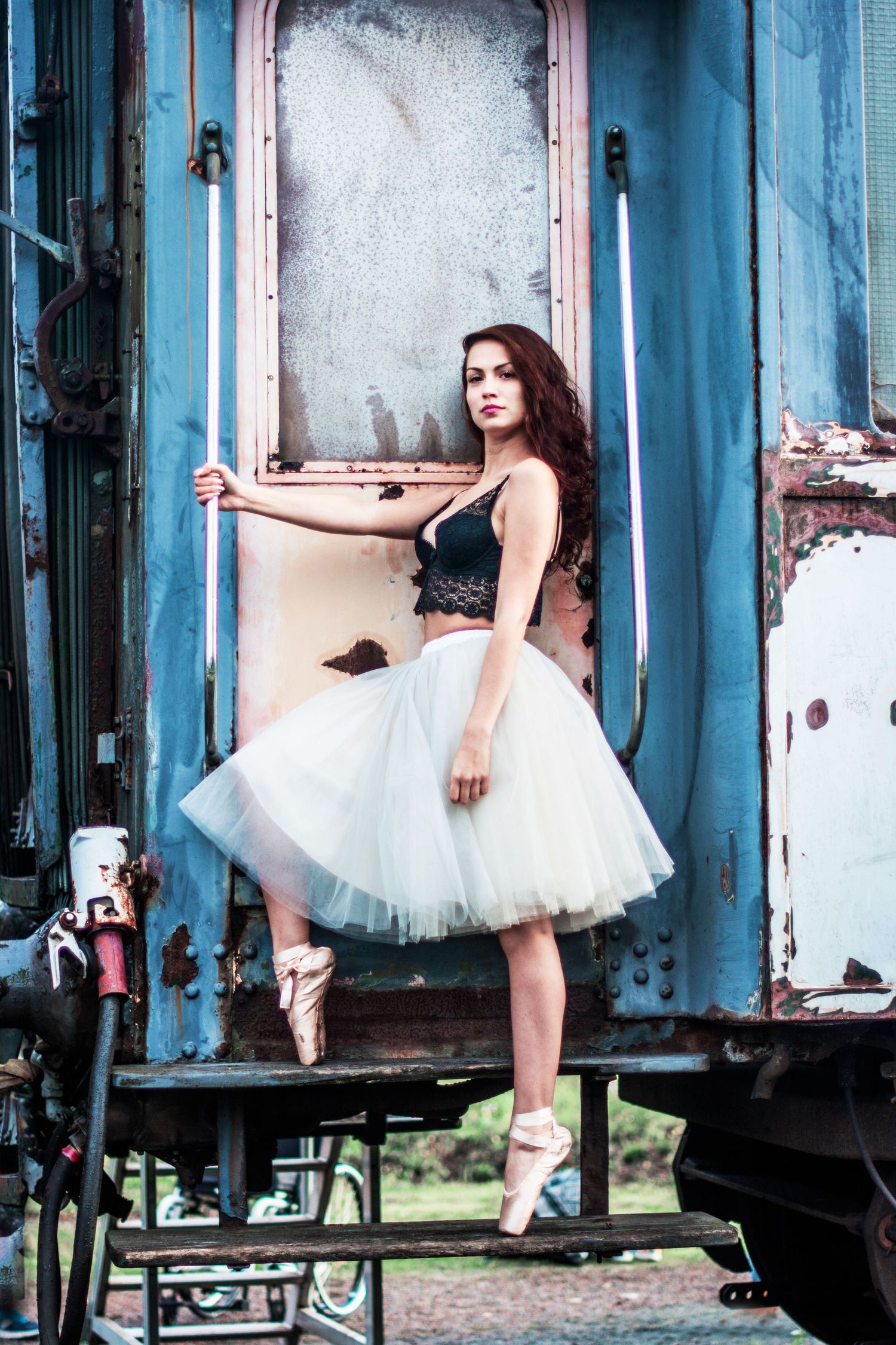 Ballerina in white tutu performs elegant poses against blue vintage train car.