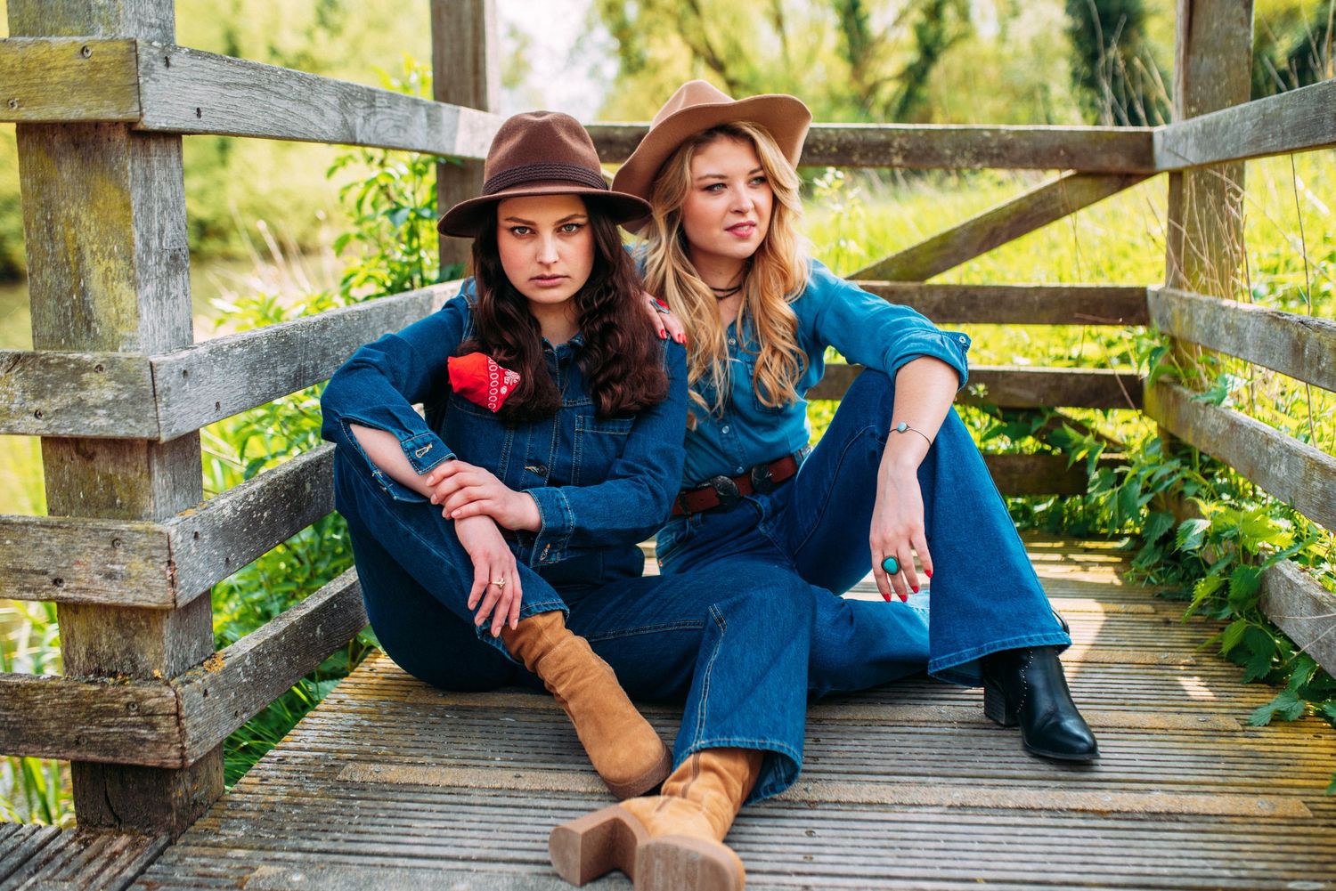 Casual portrait of two people in coordinated denim and boots lounging on wooden deck railings.