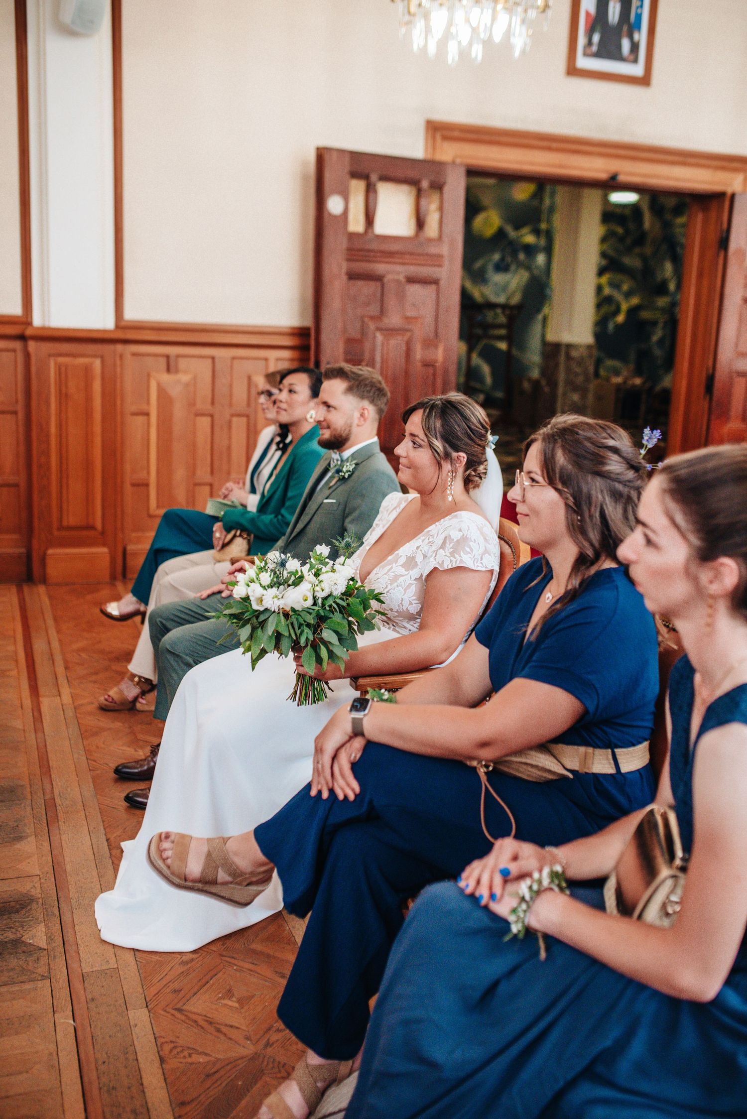 Bridesmaids in navy blue dresses react emotionally during wedding ceremony.