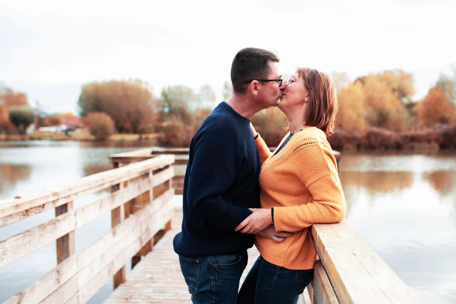 Couple sharing kiss on wooden pier during autumn sunset.
