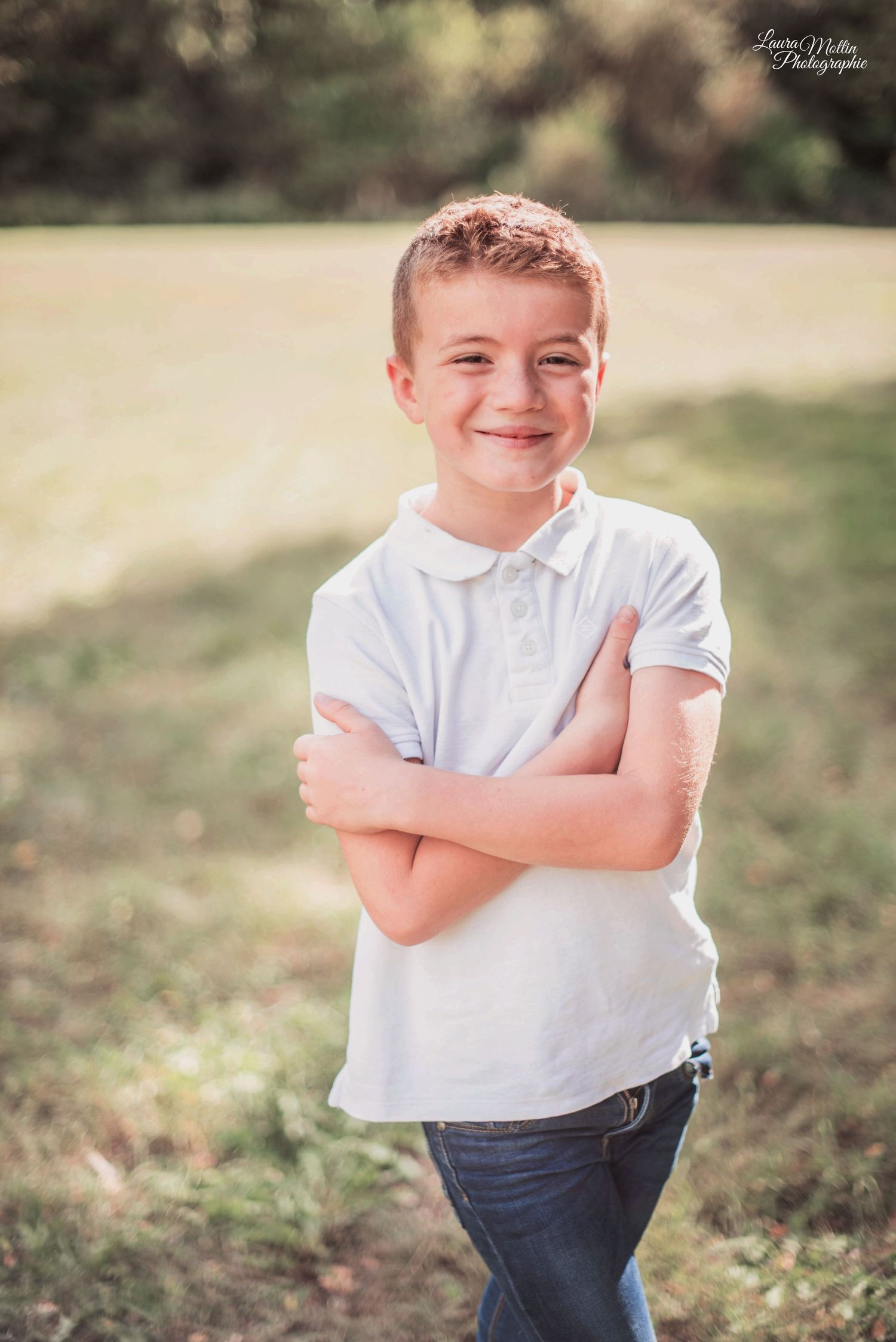 Young child in white shirt and jeans poses outdoors in natural lighting.