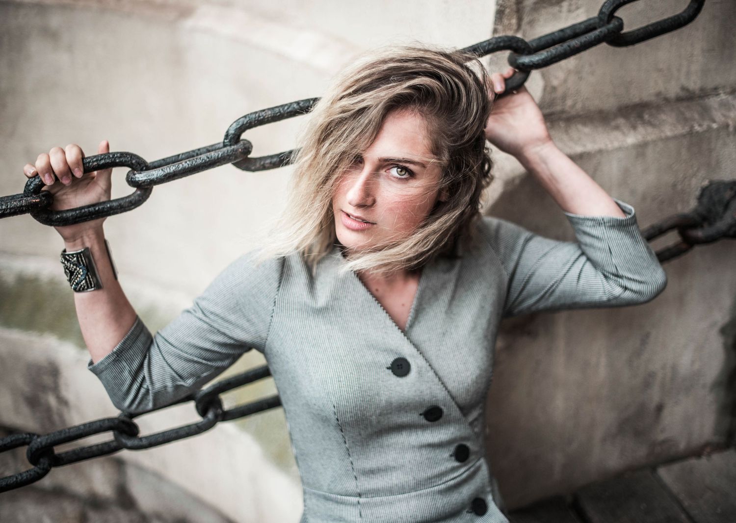 Dramatic portrait with industrial chains against concrete wall in muted tones.