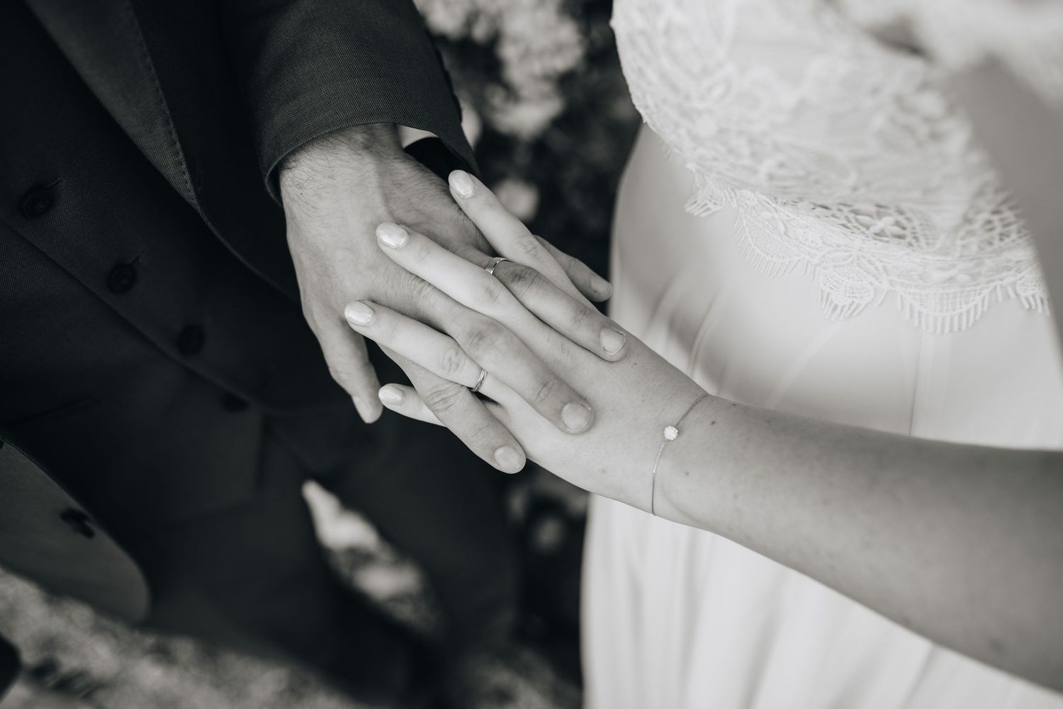Close-up details of wedding rings and hands in black and white photography.