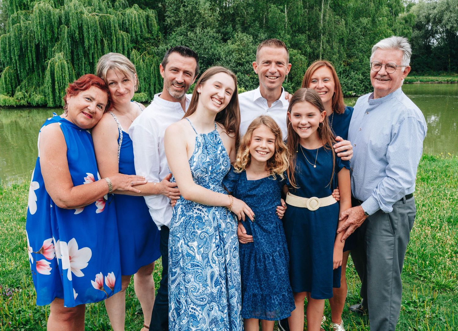 Extended family gathering in park with people wearing coordinated blue and white outfits.