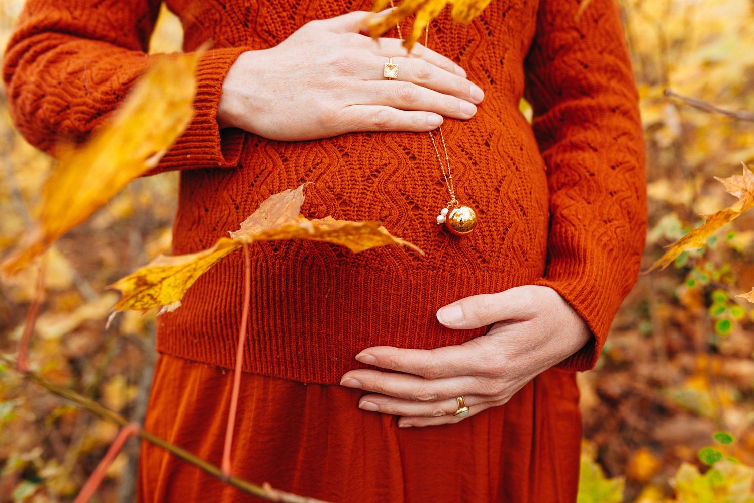 Close-up details of a burgundy sweater against autumn foliage background.