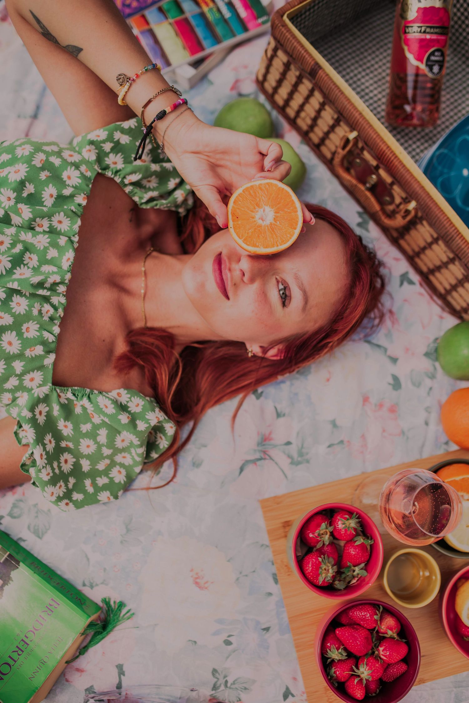 Overhead view of a picnic setup with strawberries, oranges and drinks on a white blanket.