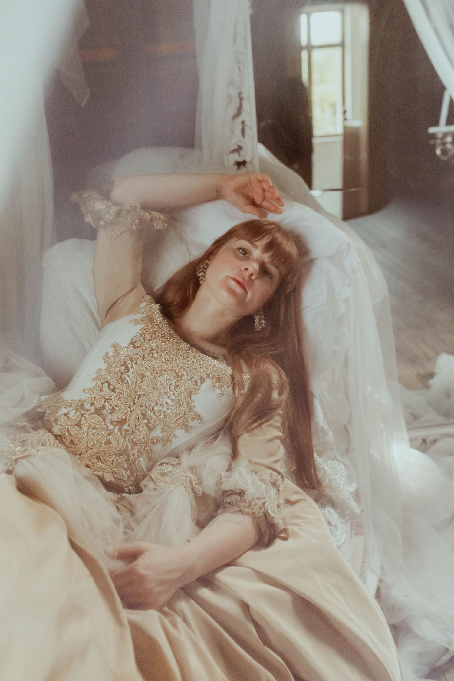 Ethereal portrait in lace dress lying among soft white fabrics.