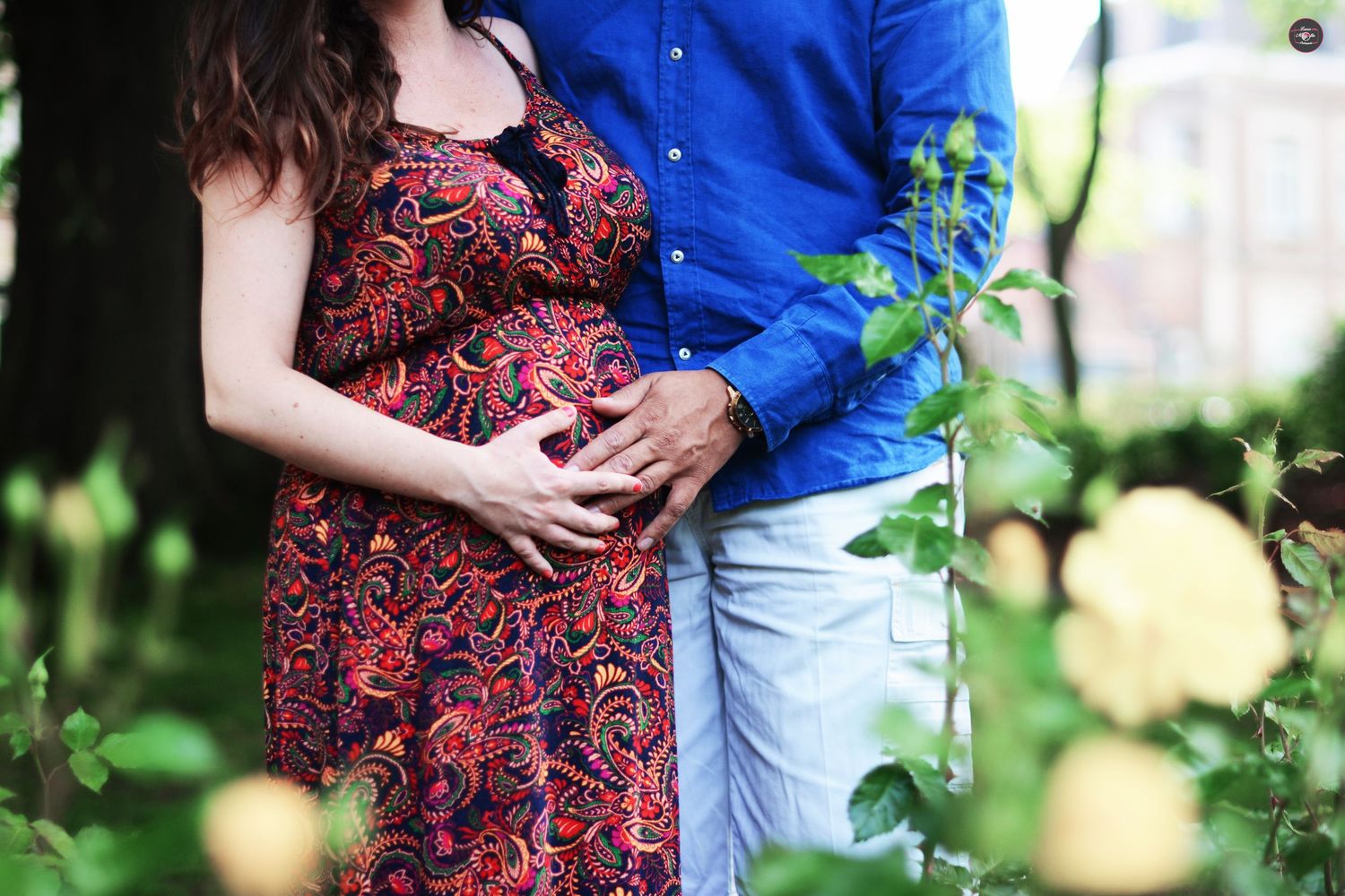 Couple embracing in garden setting with blue shirt and patterned dress.