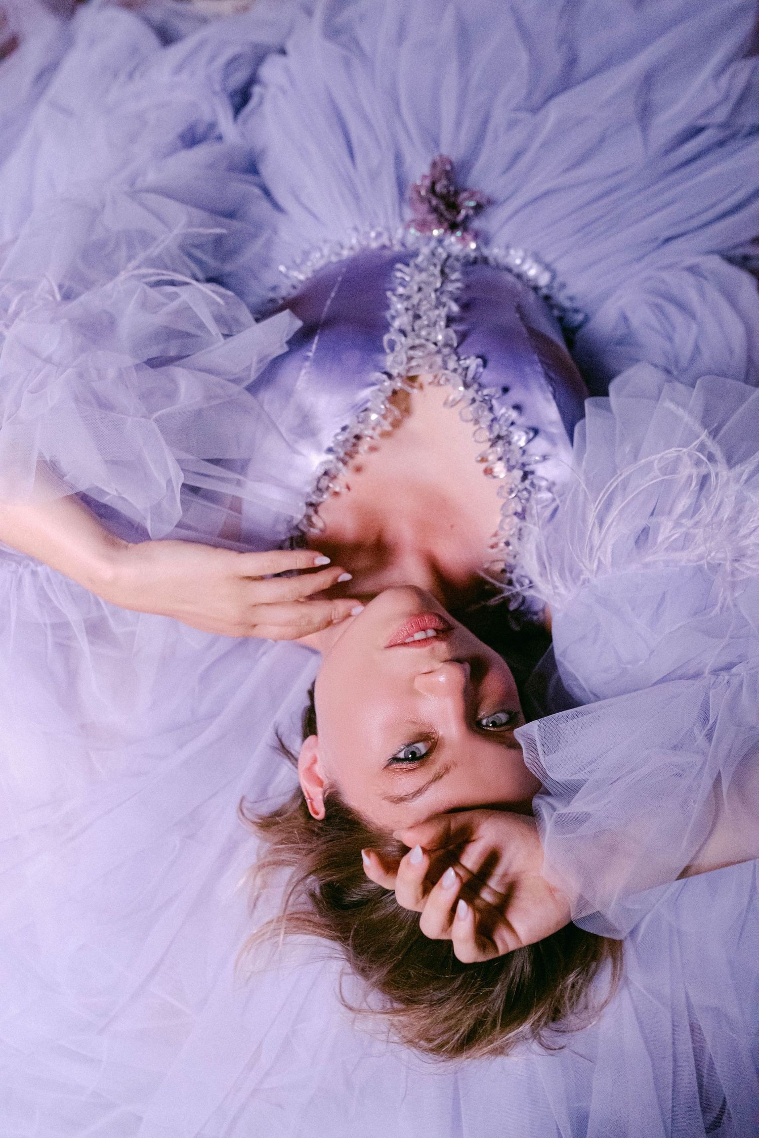 Dreamy portrait in a lavender tulle gown with crystal accessories against purple backdrop.