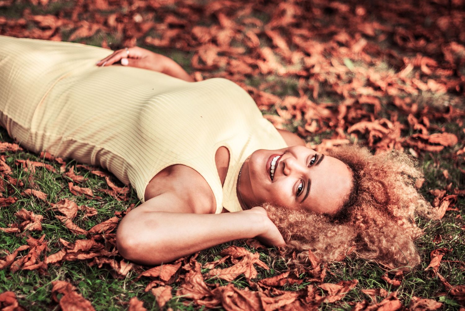Portrait lying in autumn leaves wearing cream colored sweater.