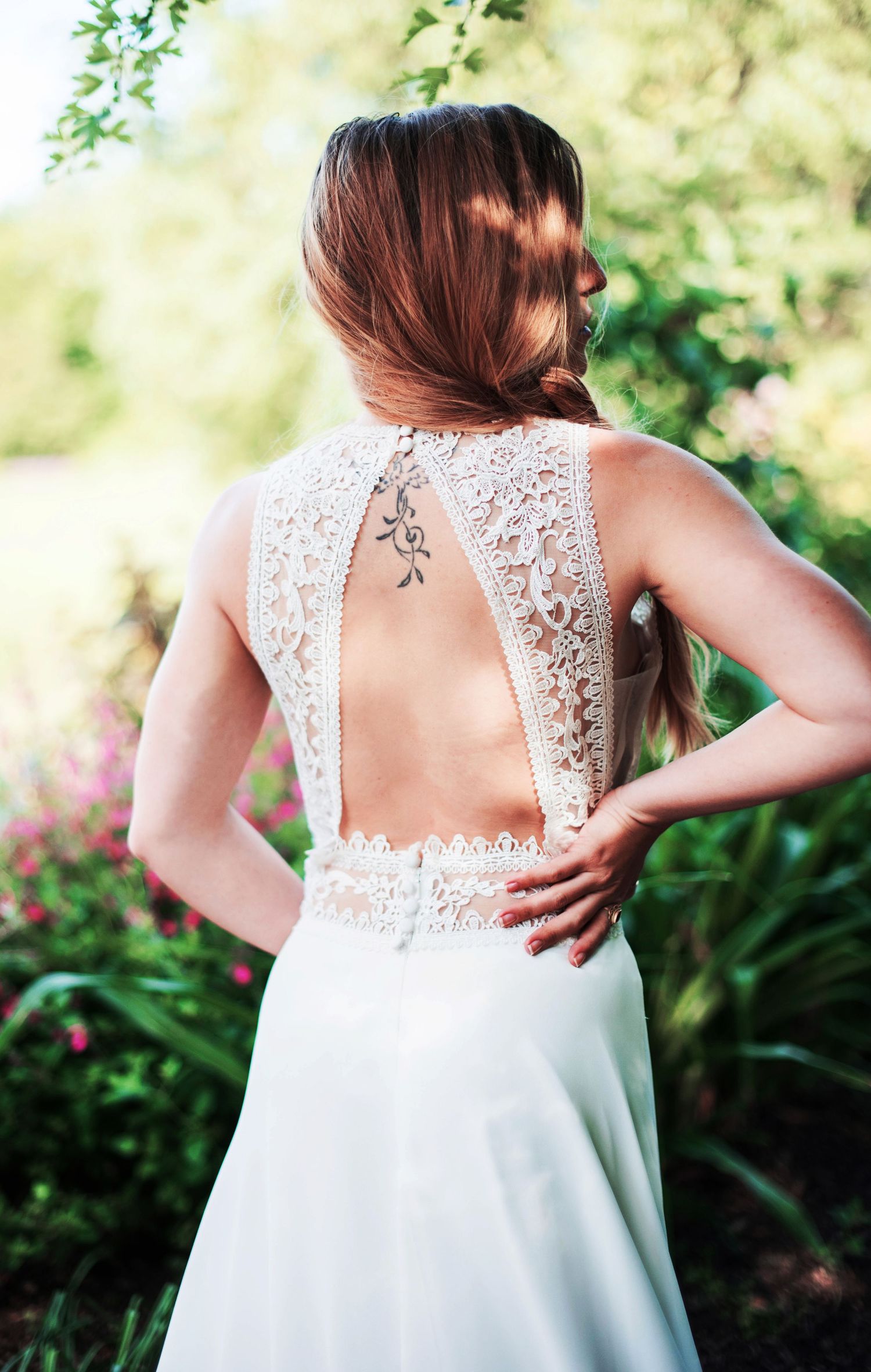 Close-up details of a white lace wedding dress back with intricate floral patterns against a garden backdrop.