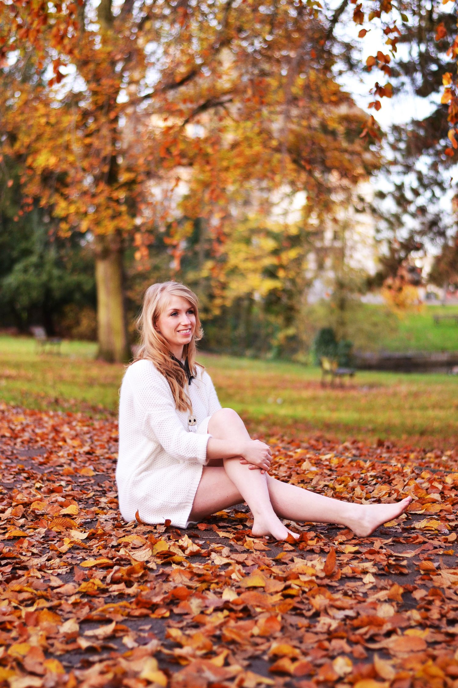 Cozy fall photoshoot with person in white sweater surrounded by orange leaves.