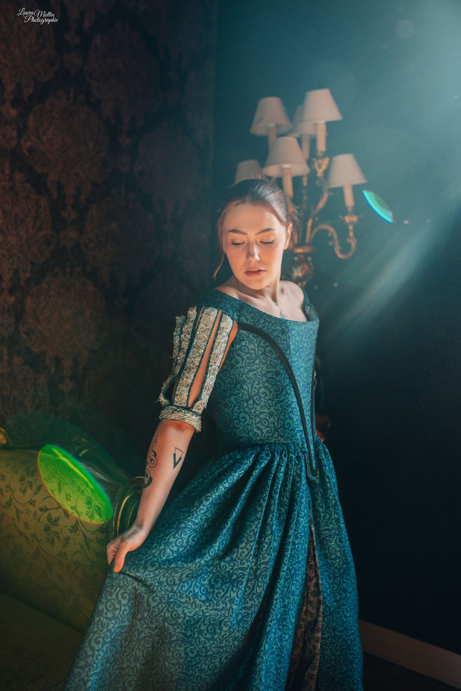 Atmospheric scene of someone in a sparkly teal vintage dress with wall sconces in the background.