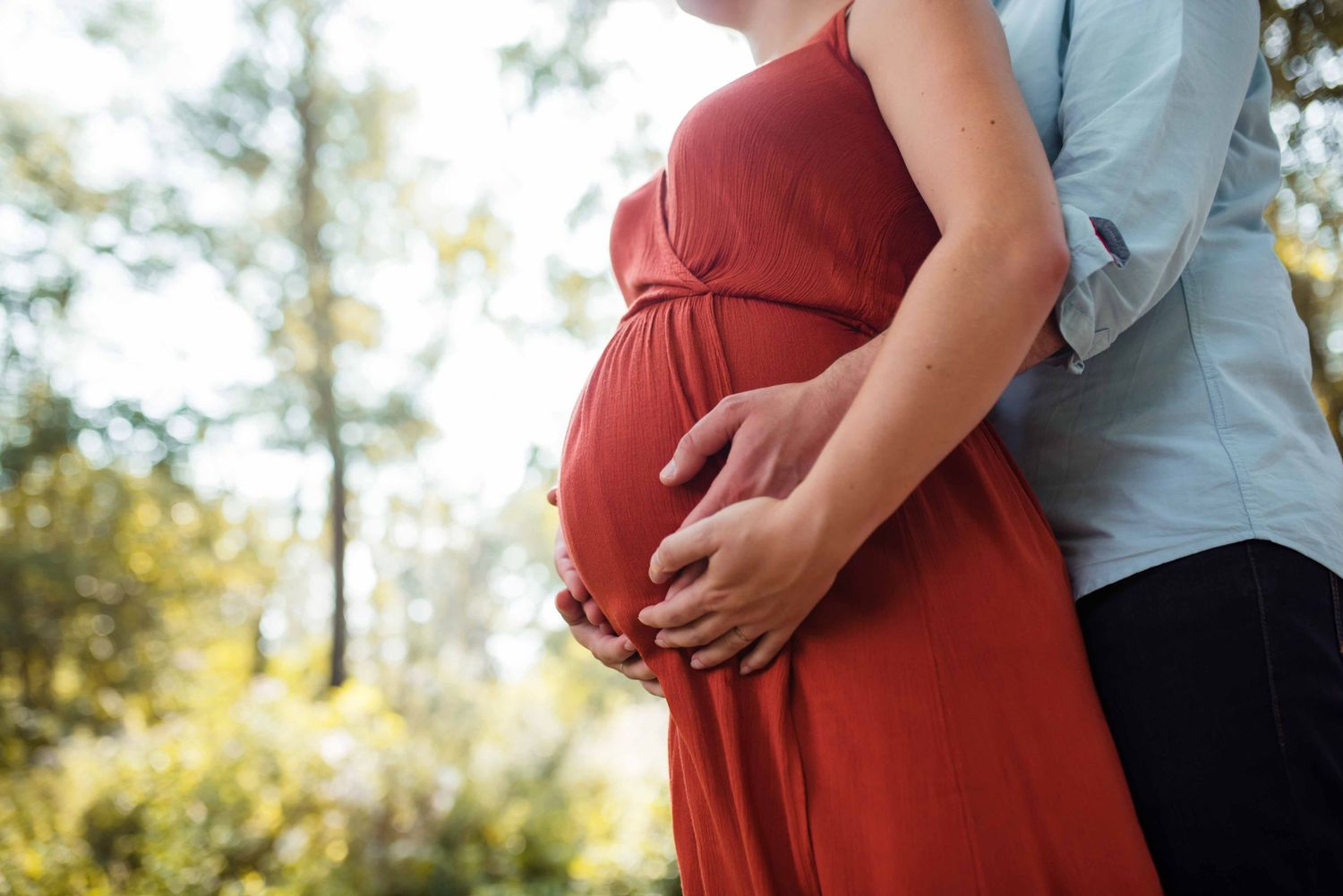 Maternity photos showing close-up shots of a pregnant belly in a red dress outdoors.