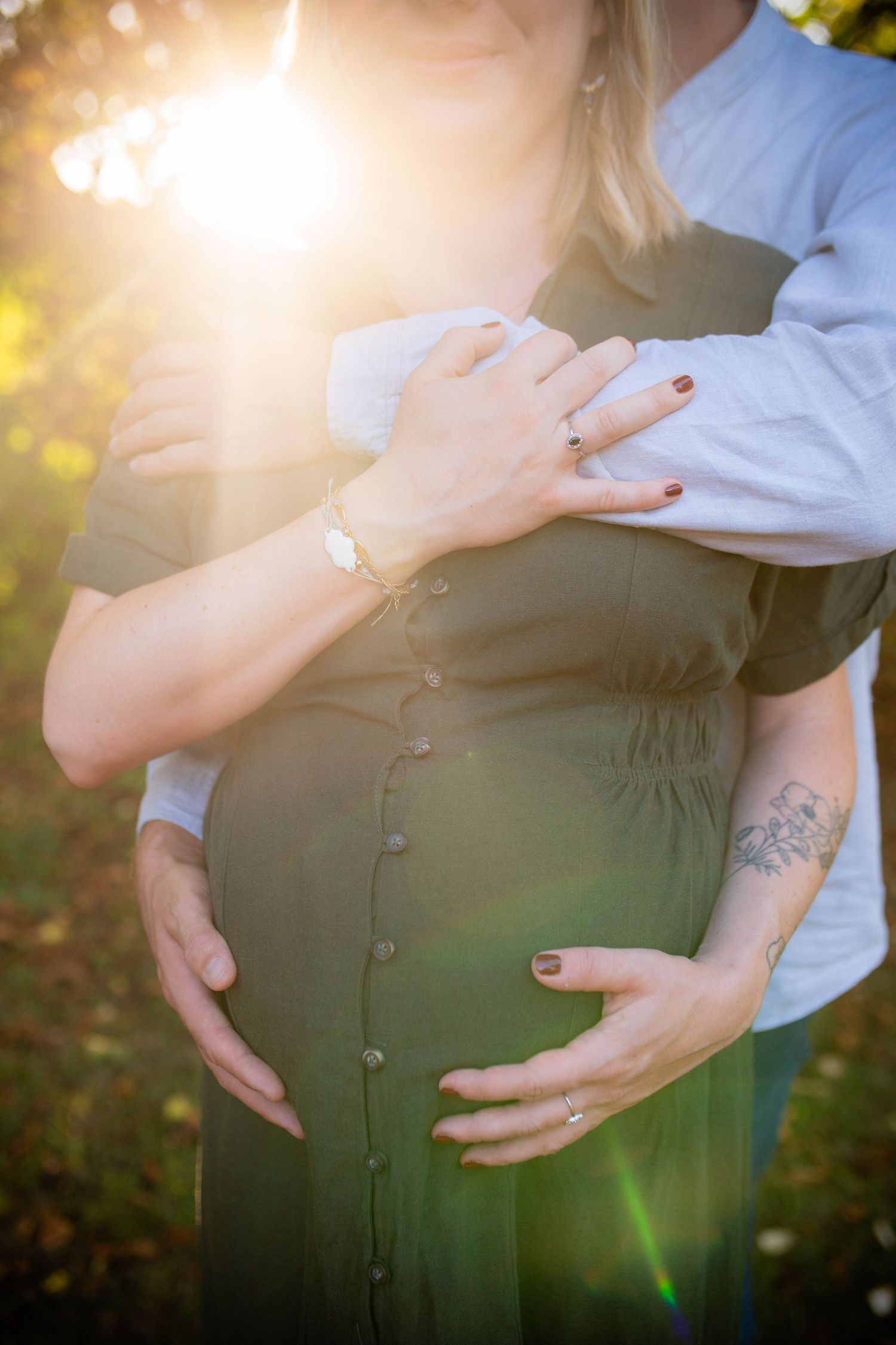 Sunlit maternity photos showing gentle hands embracing a pregnant belly in a garden setting.