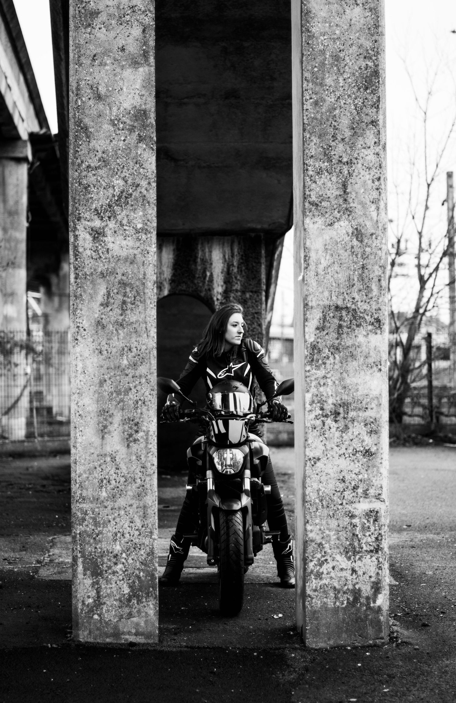 Artistic black and white photography of motorcycle between industrial concrete columns.