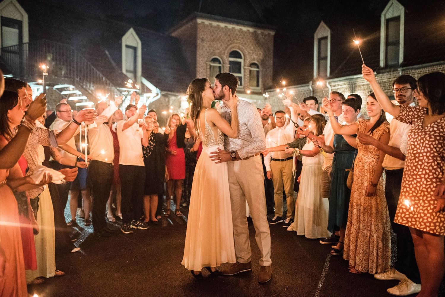 Wedding guests dance and celebrate with sparklers creating trails of light in the evening.