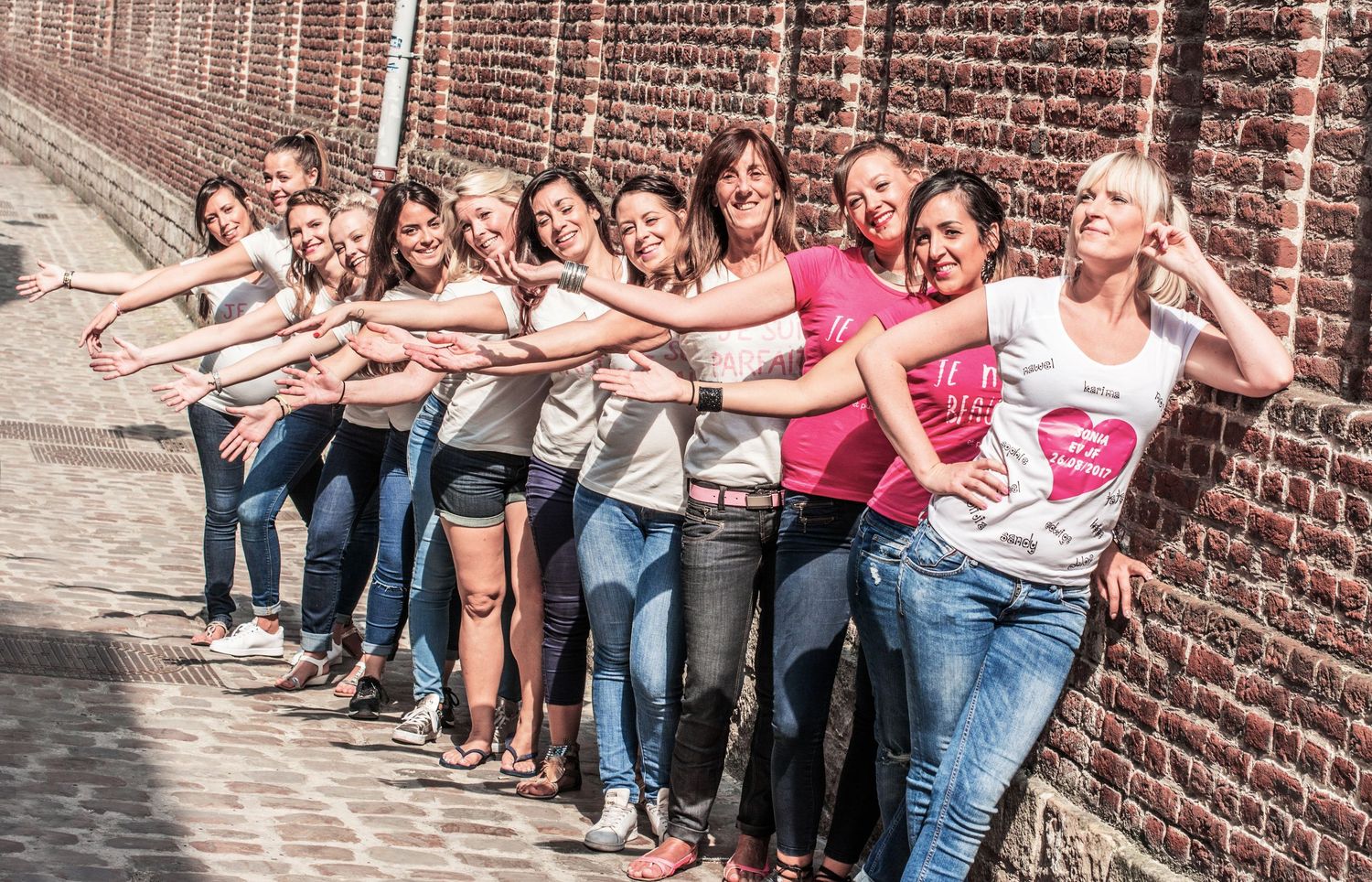Line of people leaning against brick wall in coordinated pose.