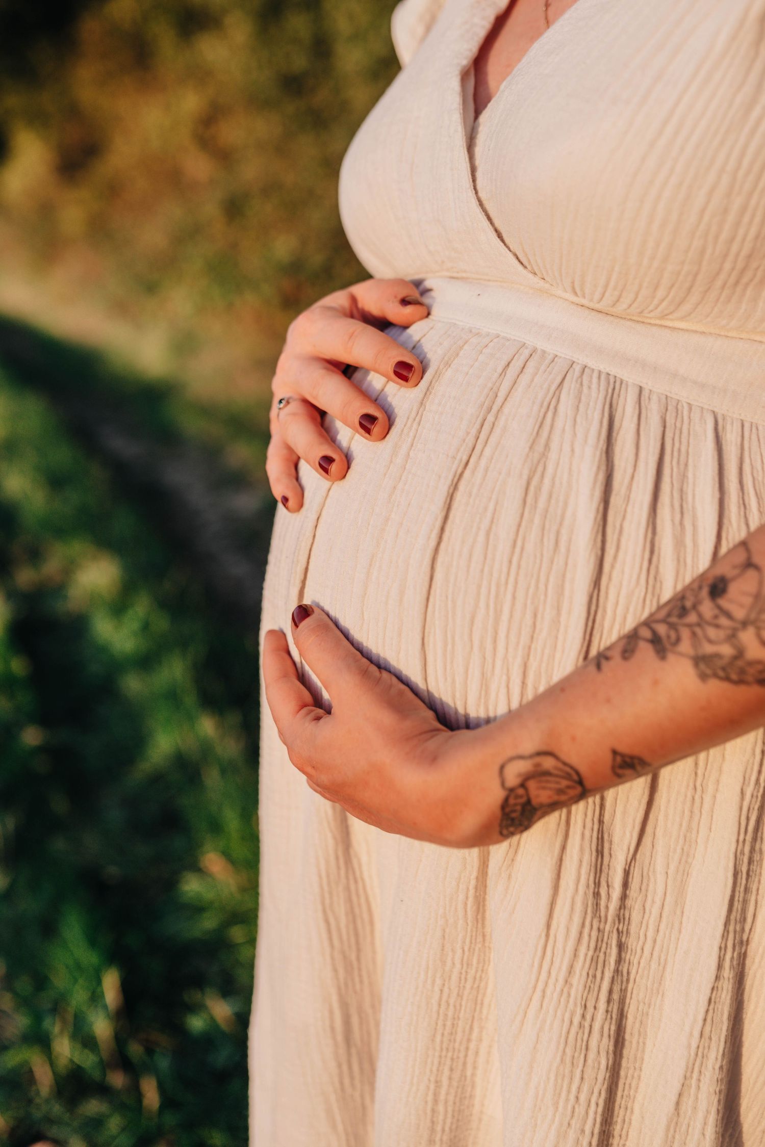 Close-up shots of tattooed arms cradling a pregnant belly in a flowing peach dress.