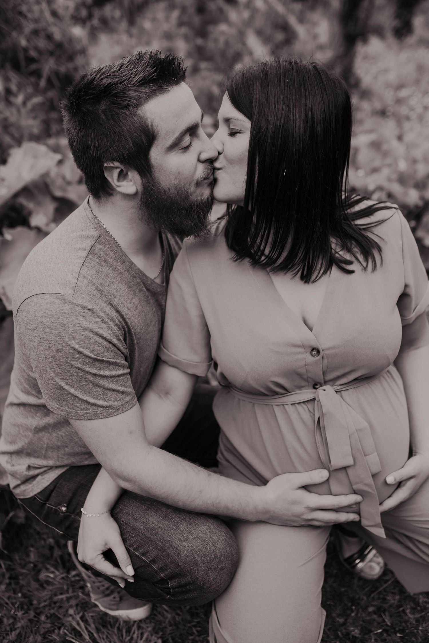 Intimate black and white maternity photo of couple sharing tender kiss outdoors.