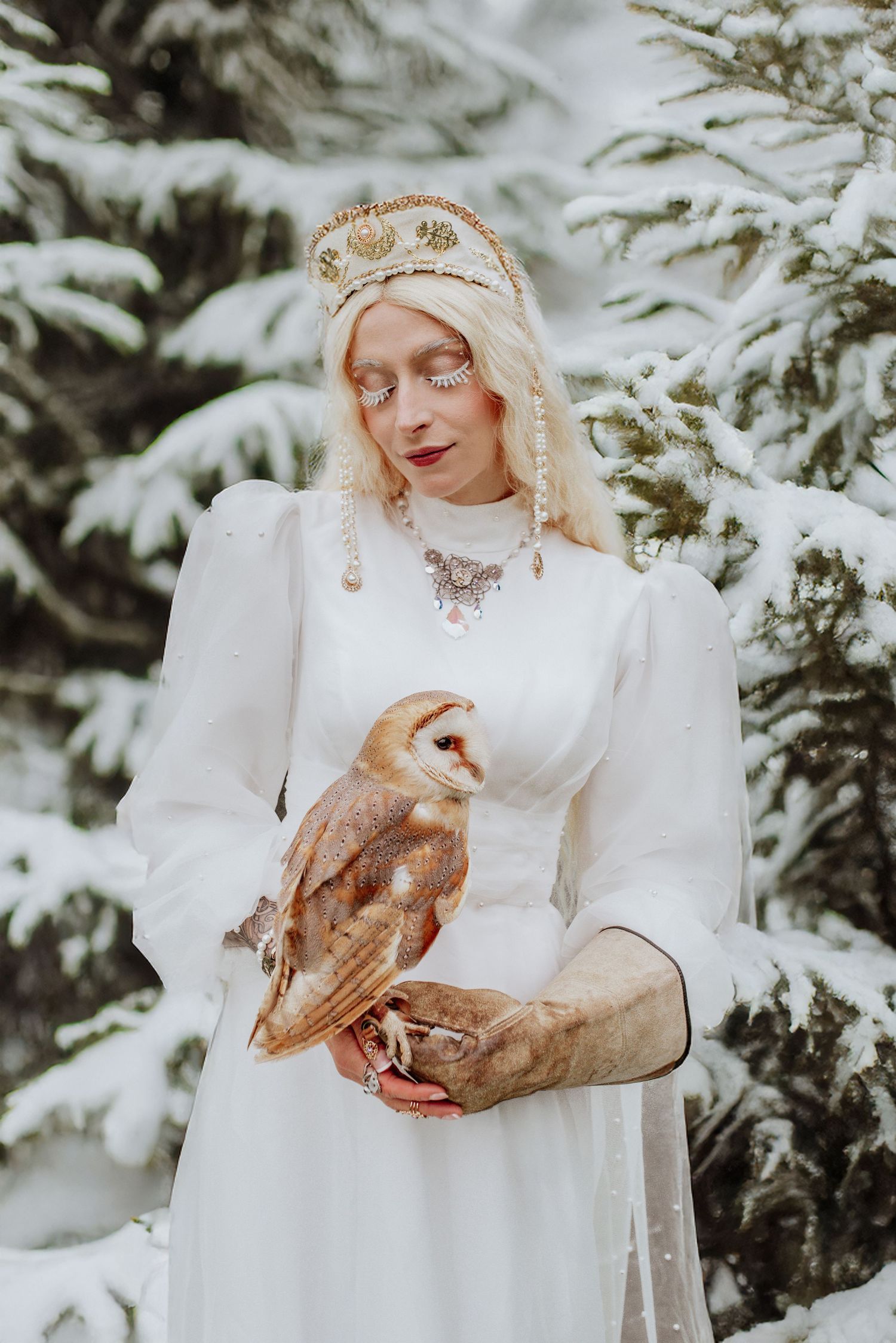 Ethereal winter portrait featuring a white gown and ornate gold headpiece against snow-covered evergreens.