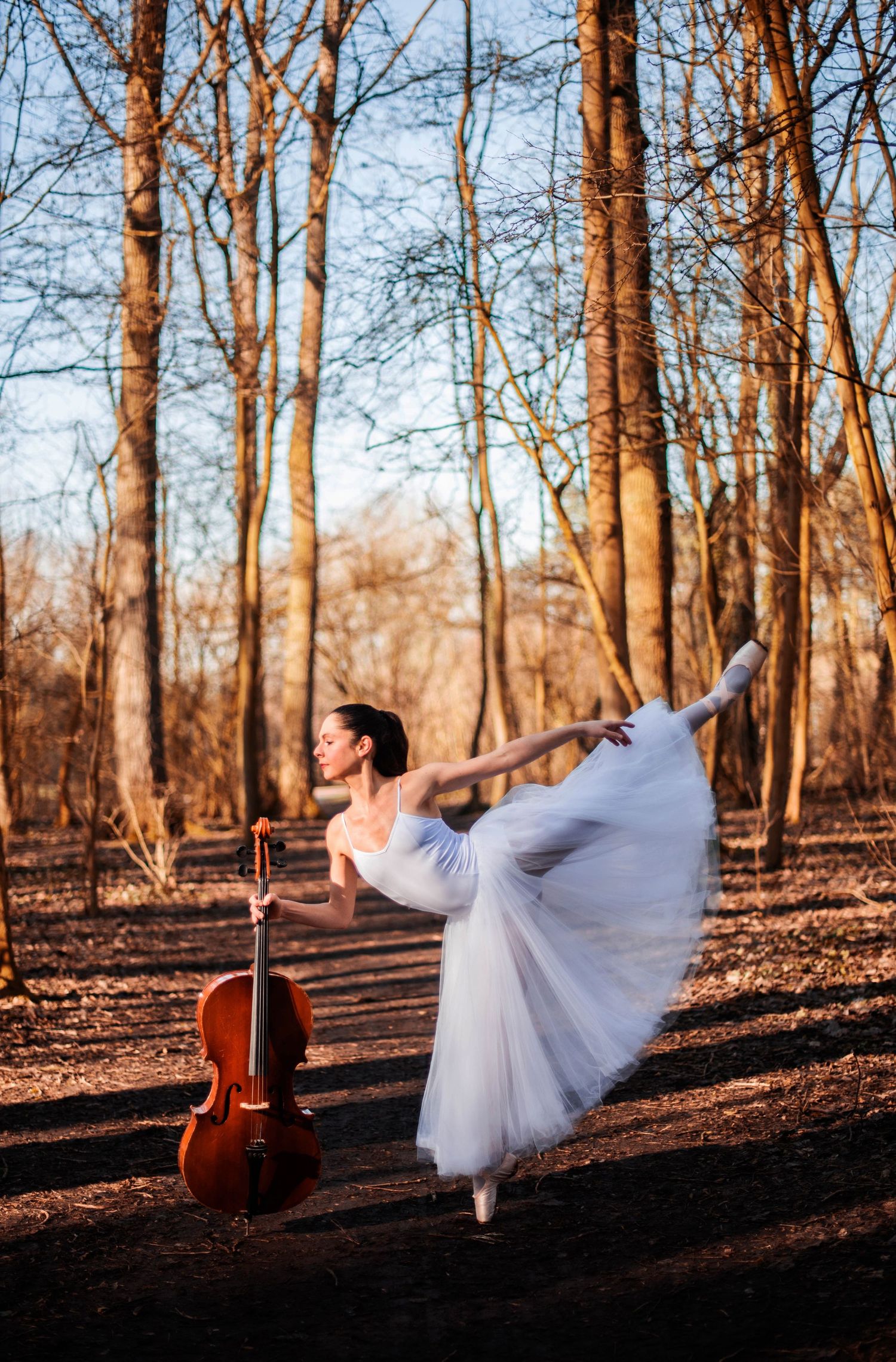 Ethereal dance movements in a white dress contrast with a cello in a sunlit forest setting.