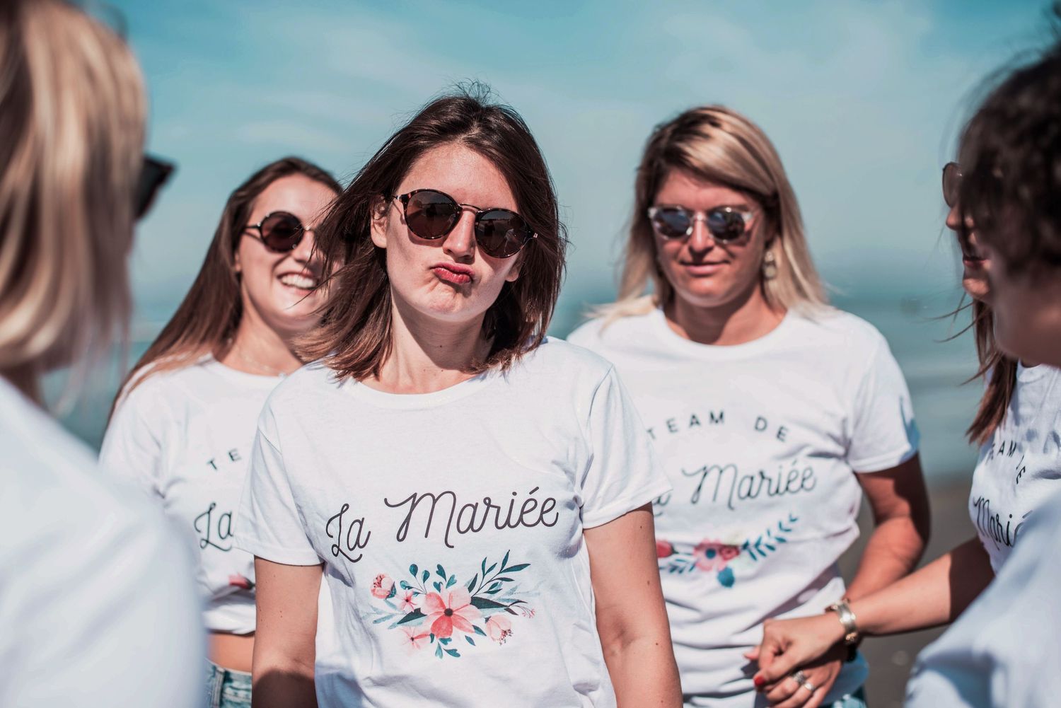 Group wearing matching white t-shirts poses together at beach celebration.