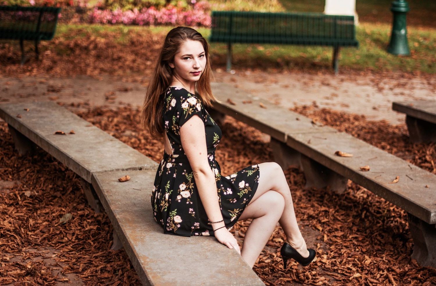 Person in a black floral dress poses on autumn leaves near stone steps.