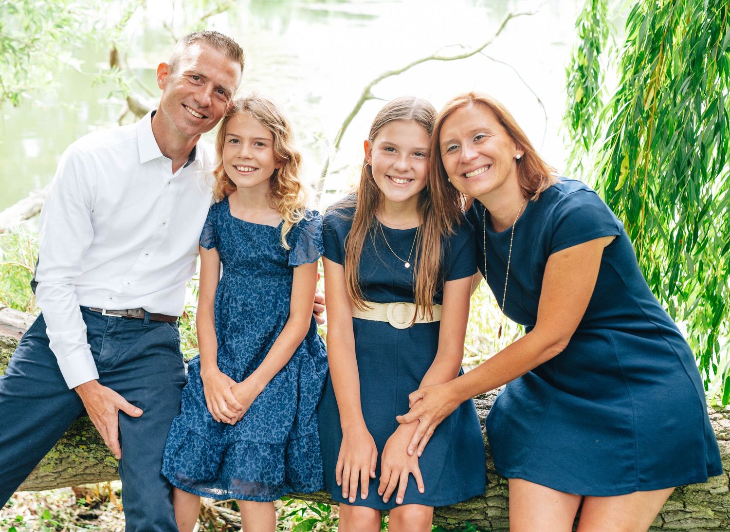 Family wearing coordinated navy blue outfits posed together under willow trees.