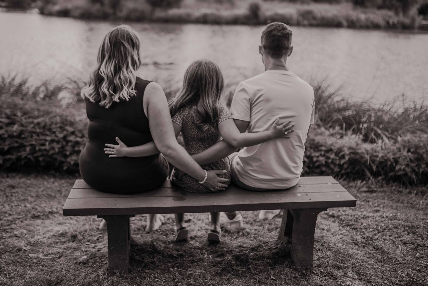 Black and white family portrait on a wooden bench in a natural setting.