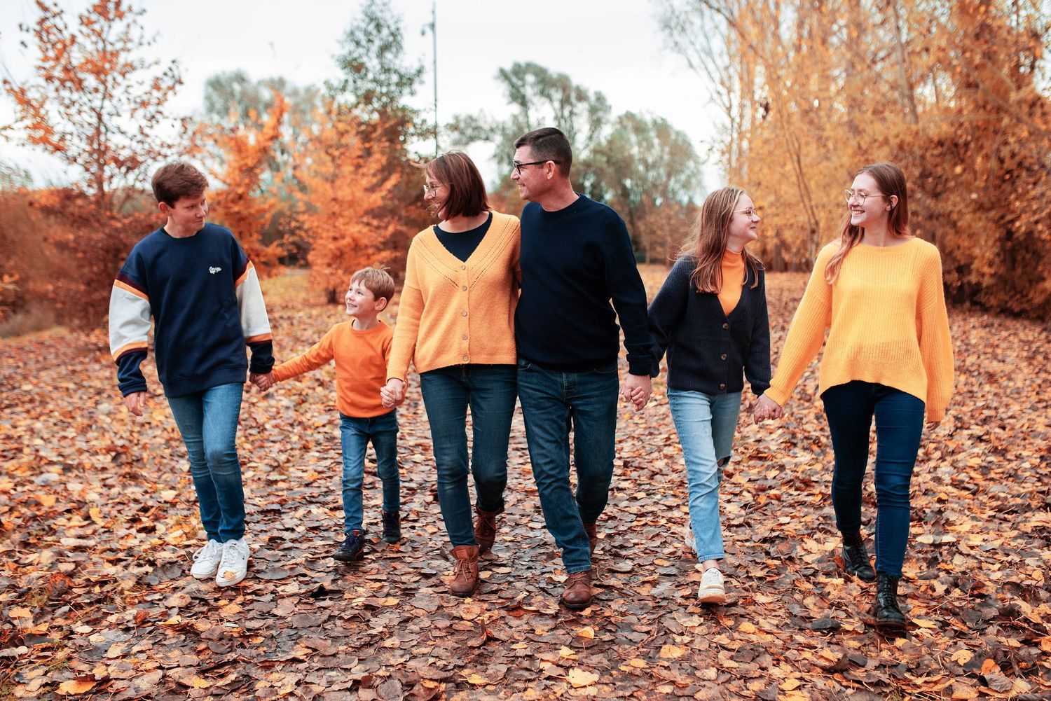 Family wearing coordinated navy and orange outfits walking through fall leaves.