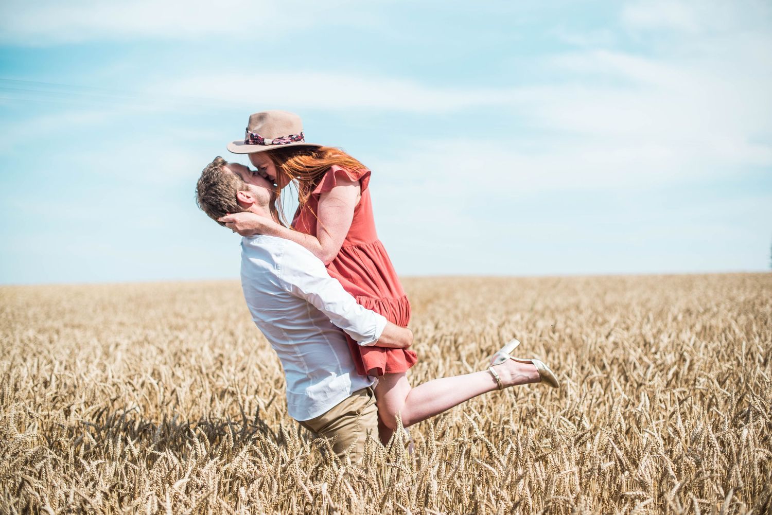 Romantic couple embracing in golden wheat field against blue sky.