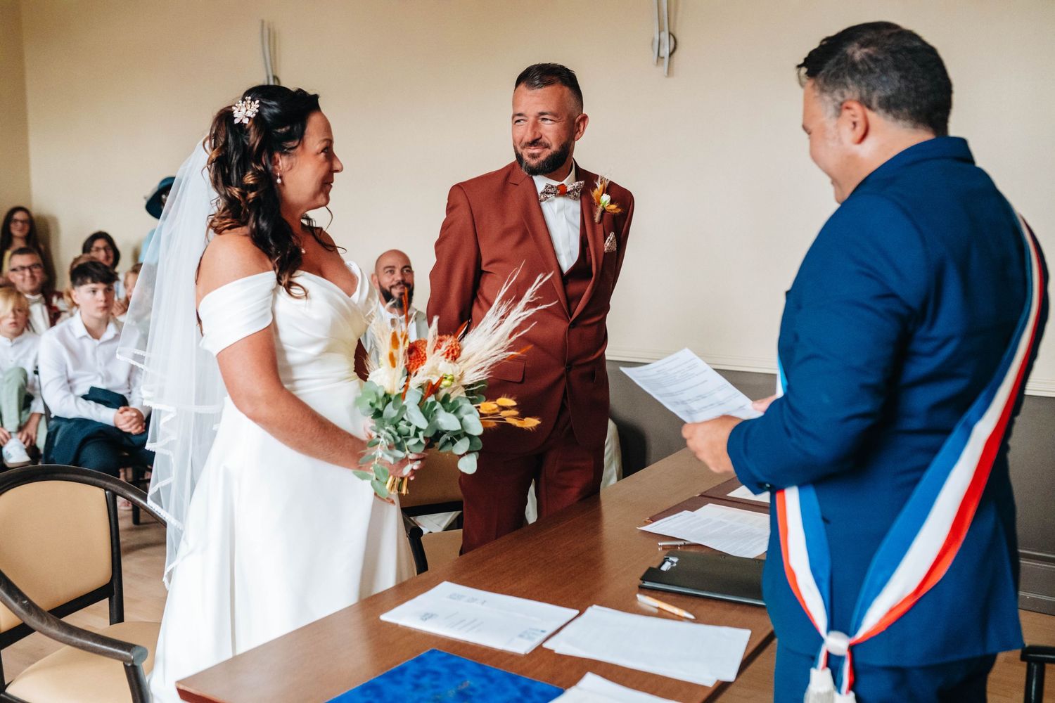 Wedding ceremony taking place in a bright indoor venue with officials in formal attire.