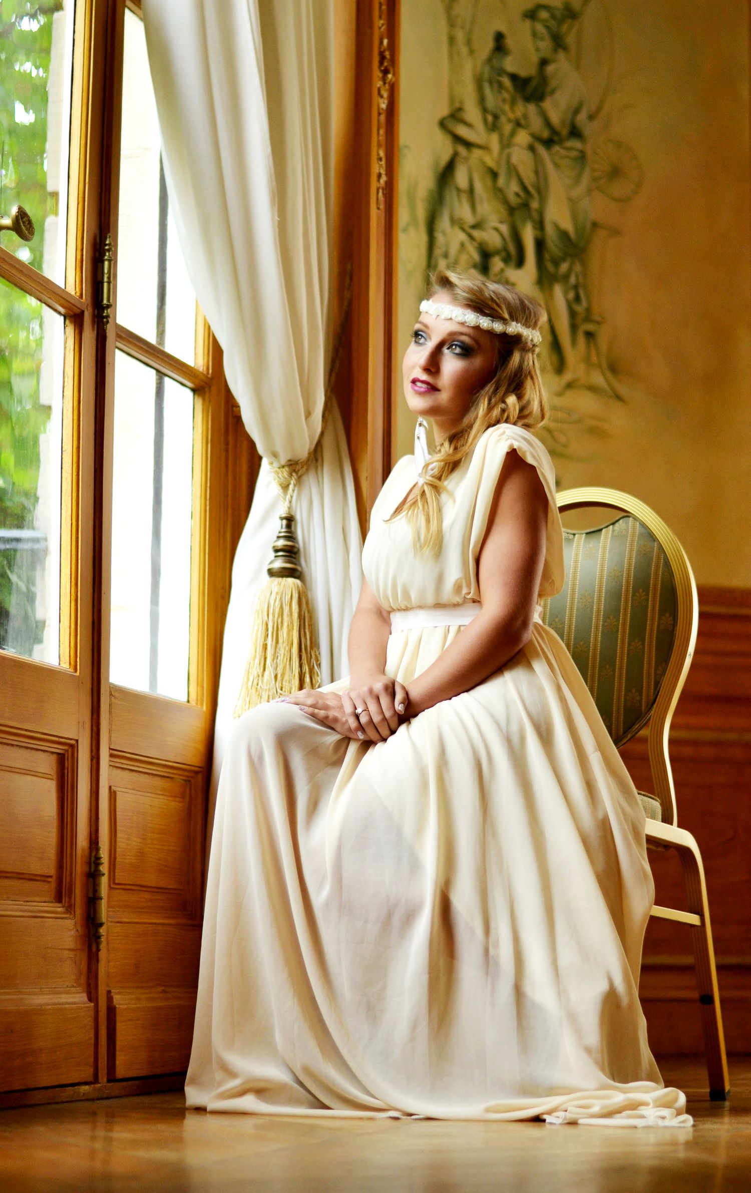 Vintage-inspired photoshoot with flowing white dress in elegant room with window.