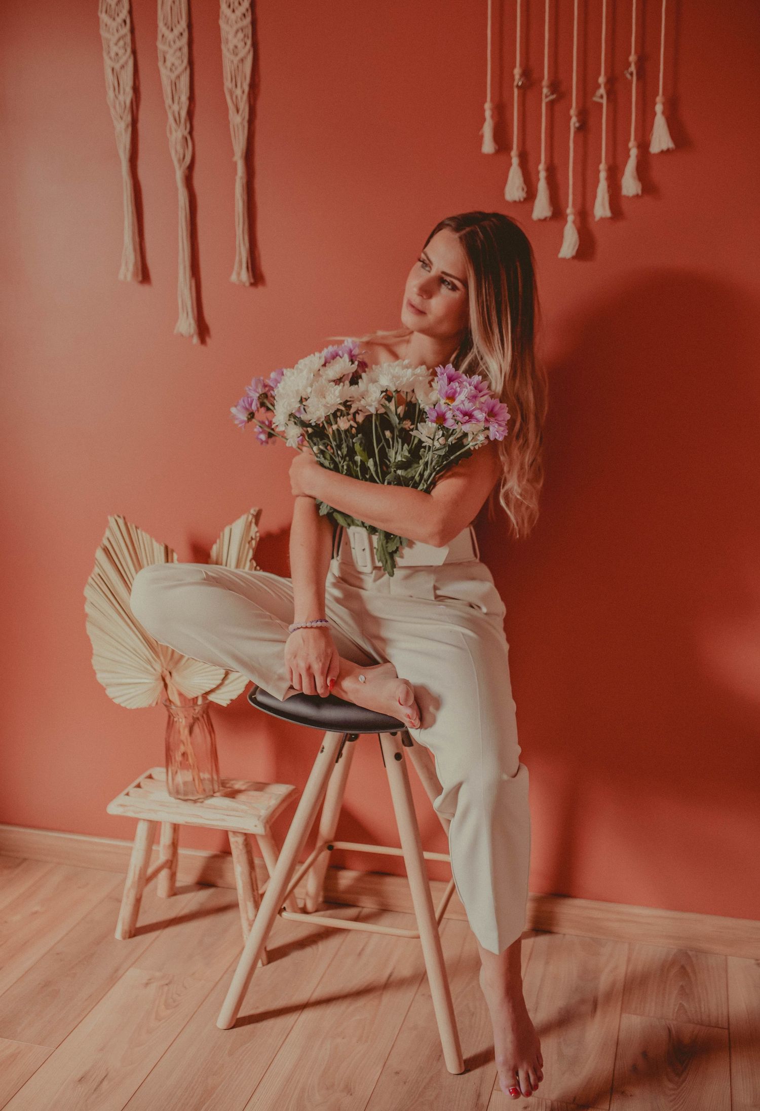 Lifestyle photos with macrame wall hanging, wooden chair, and fresh flowers in coral-toned setting.