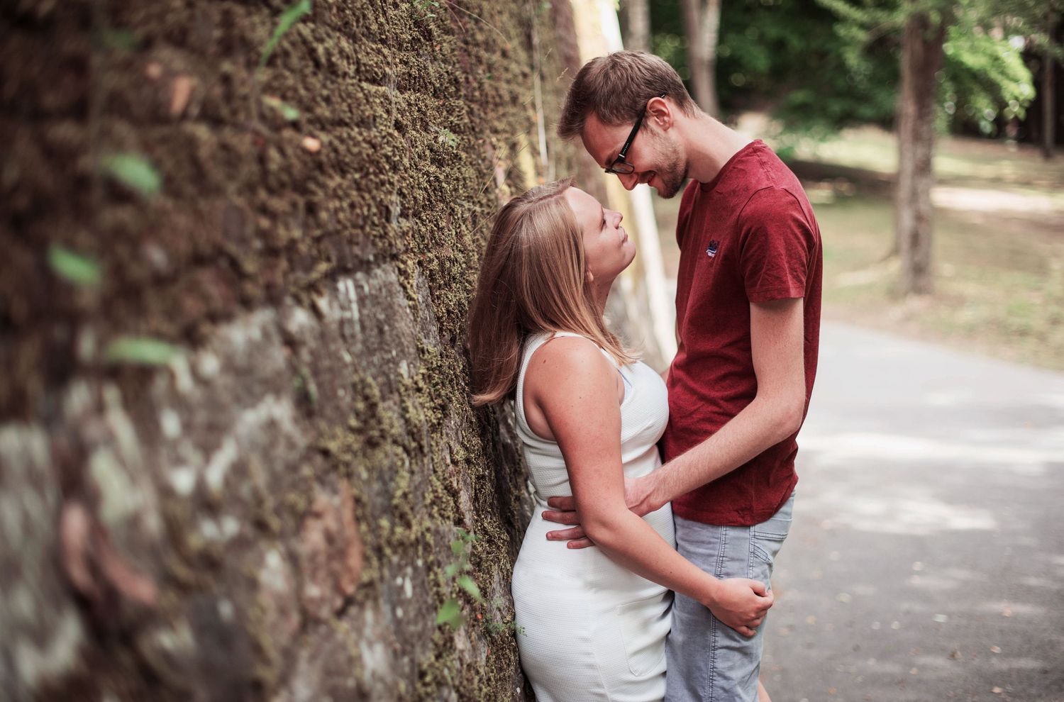 A couple embraces against a large tree trunk during an outdoor photoshoot.