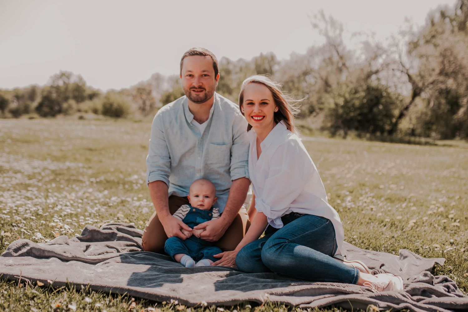 Family enjoying outdoor portrait session while sitting on blanket in grassy field.