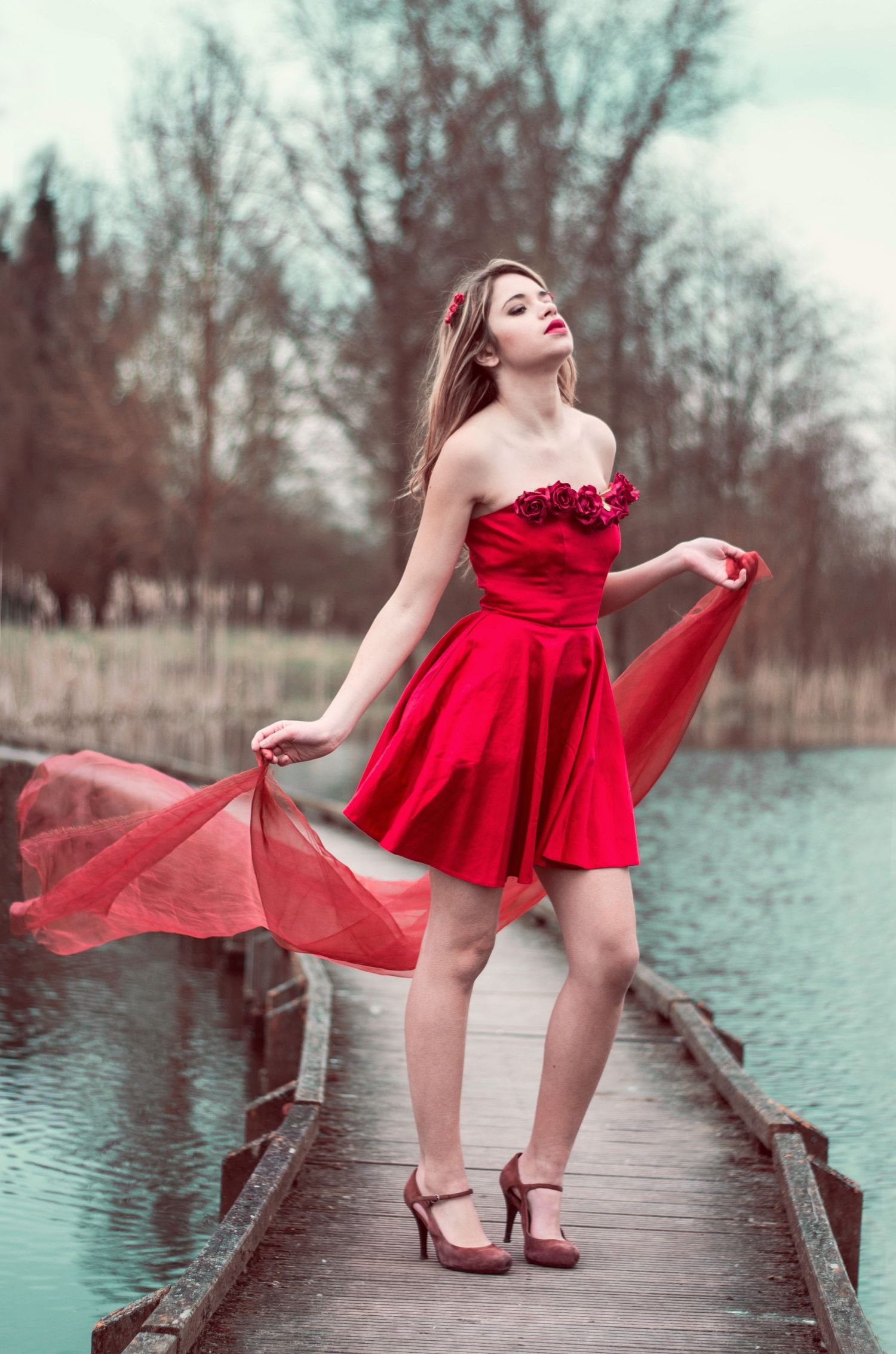 Red dress twirling on a wooden dock over tranquil turquoise water.