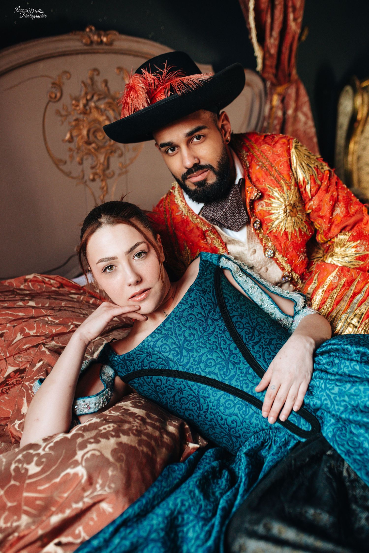 Historical costume portrait featuring ornate red and gold attire against elegant period furniture.